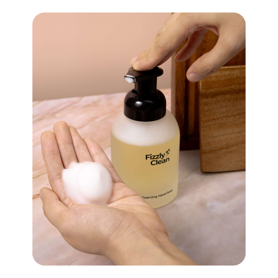 Hand holding a bottle of Fizzy Clean soap with foam on a neutral background
