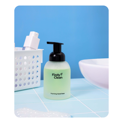 Fizzy Clean foaming hand soap bottle on a tiled bathroom floor with a blue background.