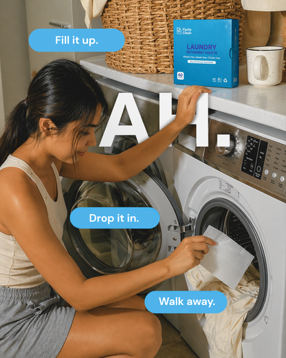 A woman kneels beside a front-loading washing machine in a laundry room, opening the door and placing a paper towel inside. A blue box labeled Pure Laundry is sitting on the counter behind her, with large overlaid text reading 'AH.