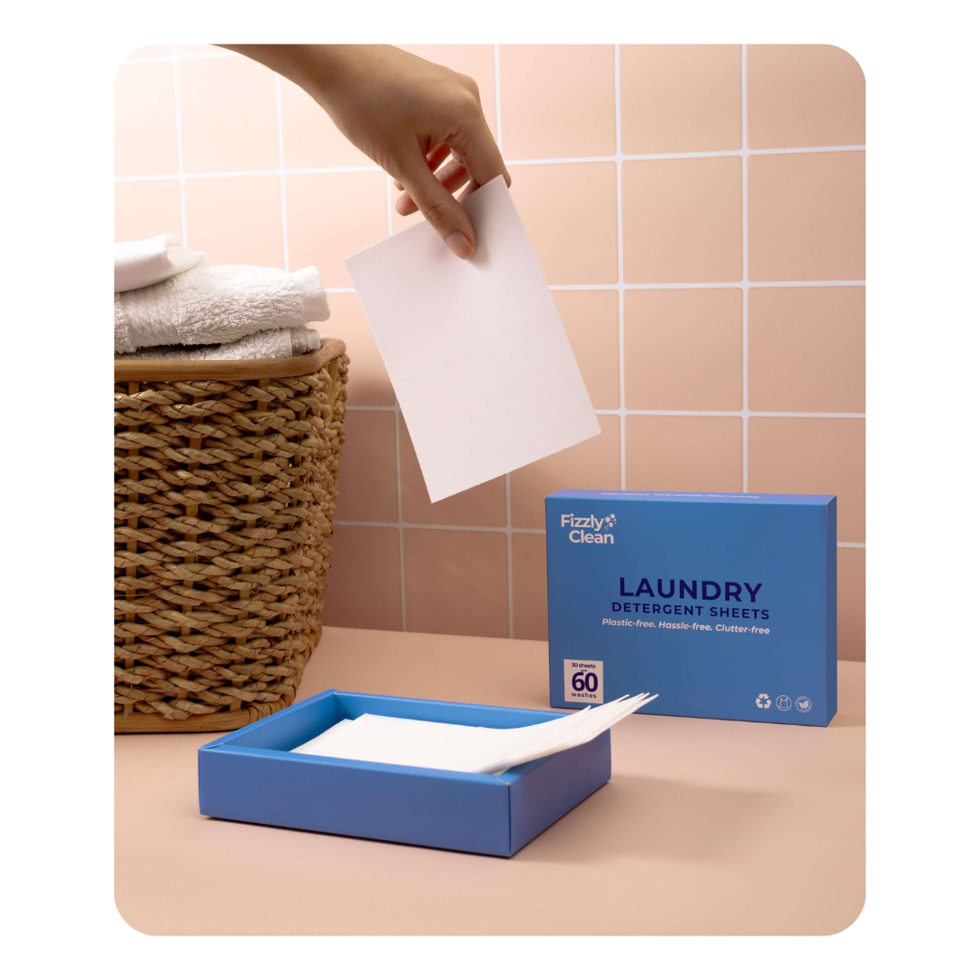 Fizzy's Clean laundry detergent sheets with a hand holding a sheet and a box on a tiled bathroom.